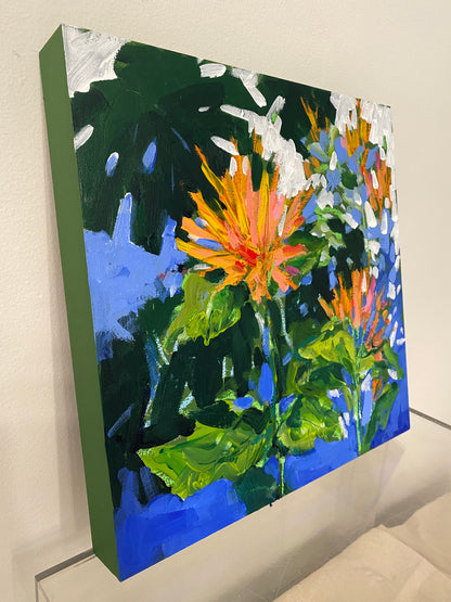 Side view of painting with dark green leaves and orange flowers against a blue background