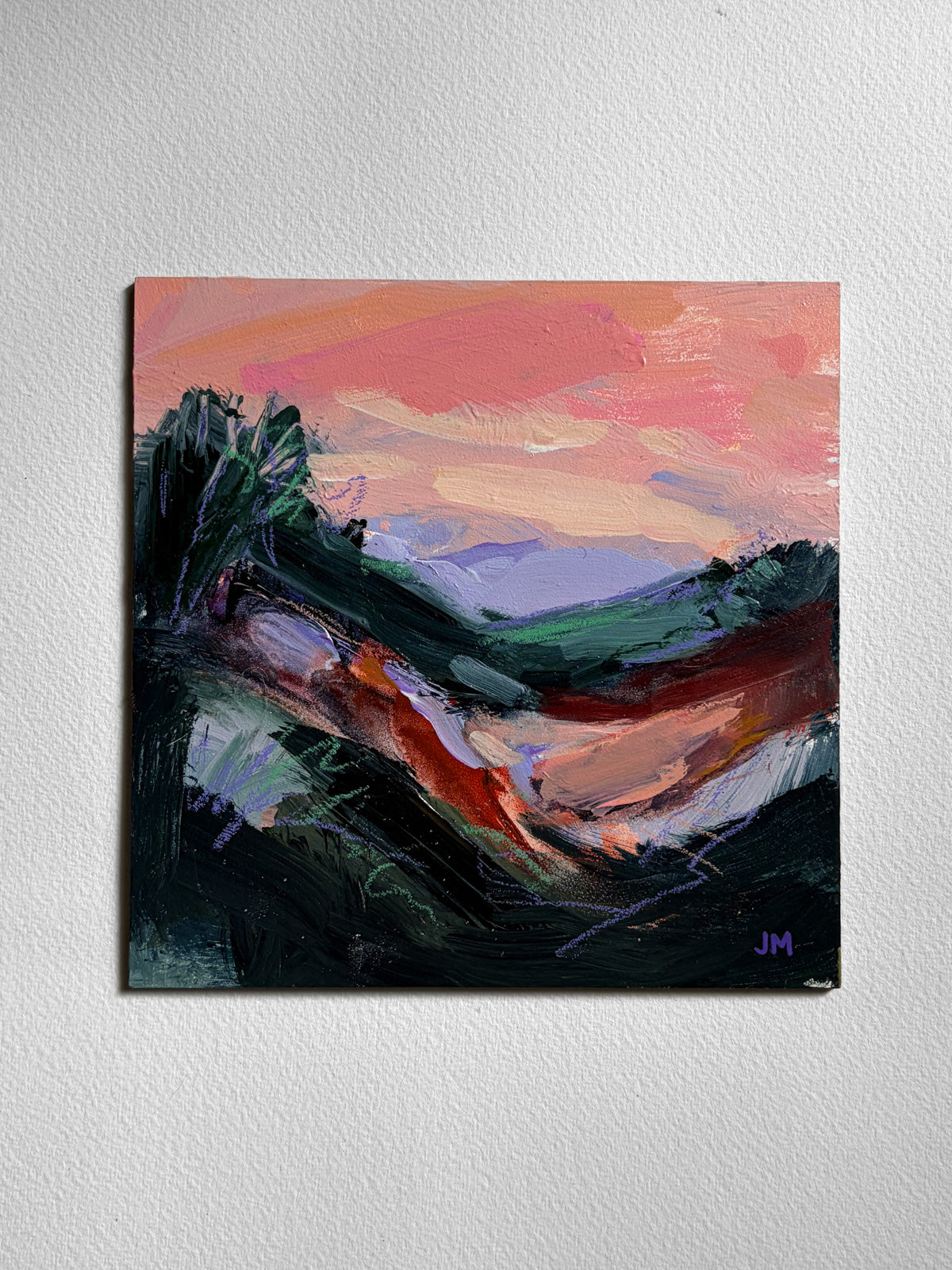 An abstract landscape painting on board, featuring a vibrant pink  sky, violet hills, and dark foreground brushstrokes, displayed on a textured white wall.