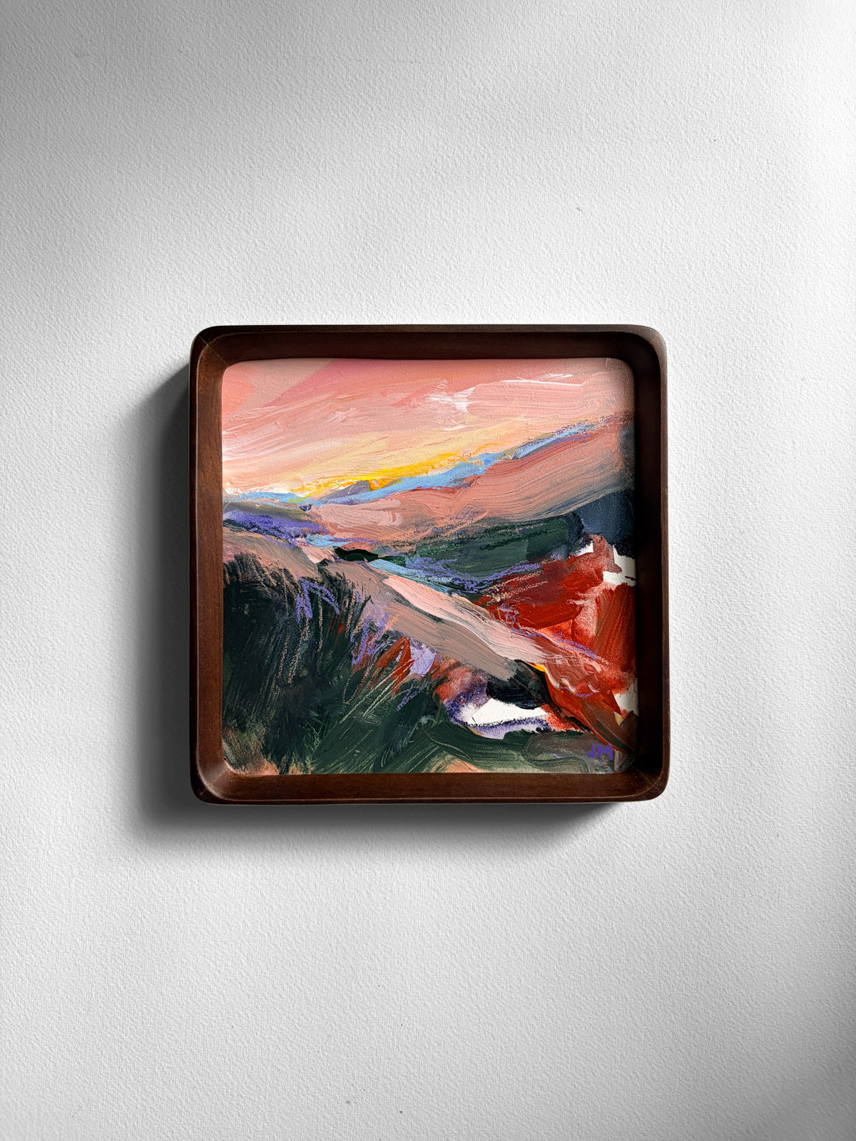 A square framed abstract landscape painting with a dark brown wooden frame, mounted on a light gray textured wall.