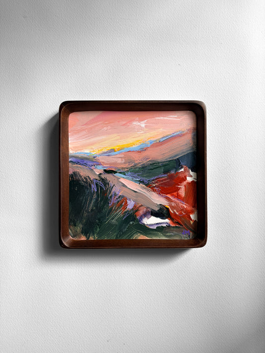 A square framed abstract landscape painting with a dark brown wooden frame, mounted on a light gray textured wall.