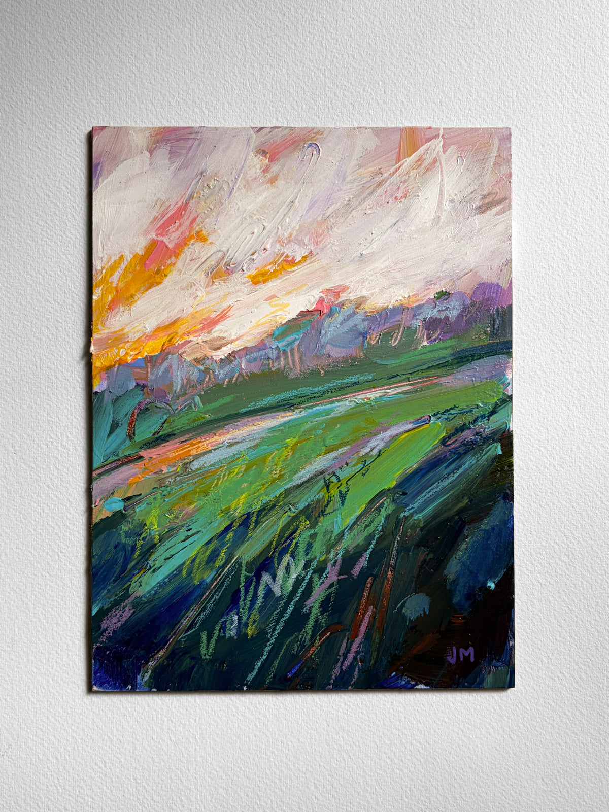 An abstract landscape painting on board, featuring a vibrant green field under a cloudy sky with orange, pink, and blue tones, displayed on a textured white wall.