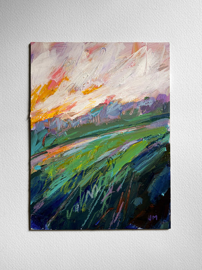 An abstract landscape painting on board, featuring a vibrant green field under a cloudy sky with orange, pink, and blue tones, displayed on a textured white wall.