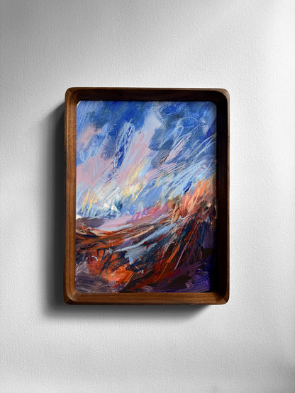 A framed abstract landscape painting featuring vibrant blue and brown brushstrokes, housed in a dark brown wooden frame and mounted on a light gray textured wall.
