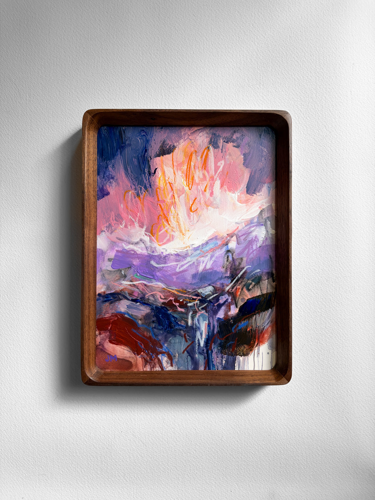 A framed abstract landscape painting featuring vibrant purple, pink, orange, and blue brushstrokes, housed in a dark brown wooden frame and mounted on a light gray textured wall.