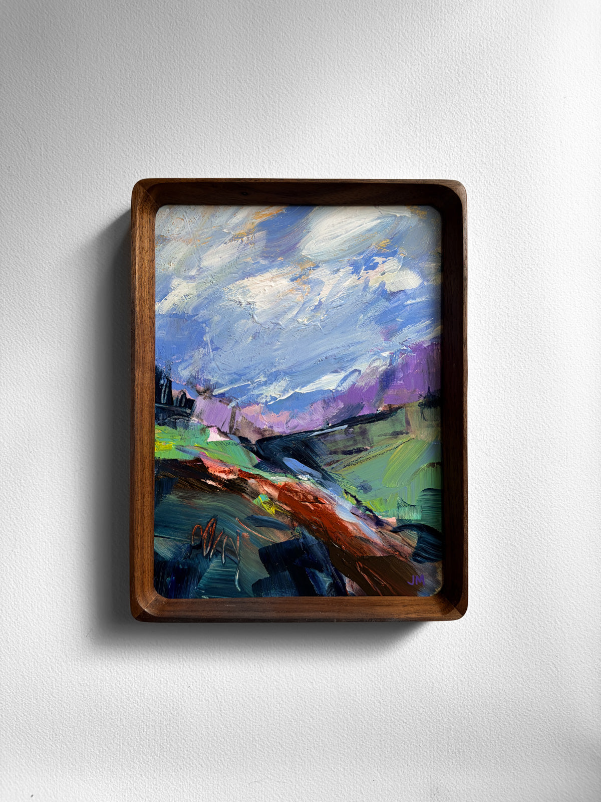 A framed abstract landscape painting featuring blue, purple, and green brushstrokes, housed in a dark brown wooden frame and mounted on a light gray wall.