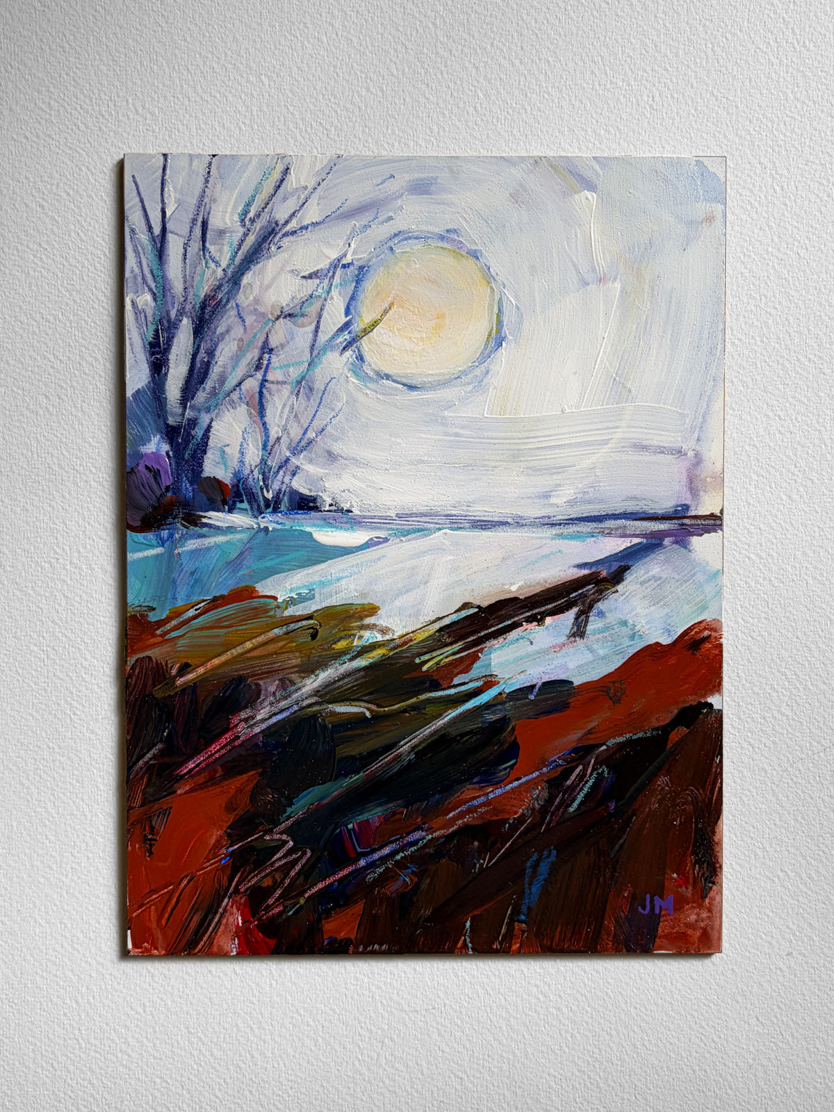 An abstract landscape painting on board, featuring a pale yellow sun or moon in a white and blue sky, dark blue bare tree branches, and a foreground of textured red, brown, and black brushstrokes, displayed on a light gray wall.