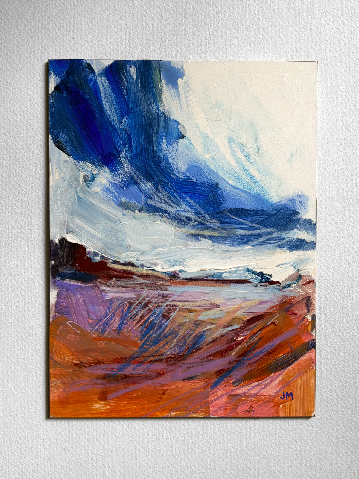 An abstract landscape painting on board, featuring a dramatic blue and white sky above a textured orange, brown, and purple ground, displayed on a light gray wall.