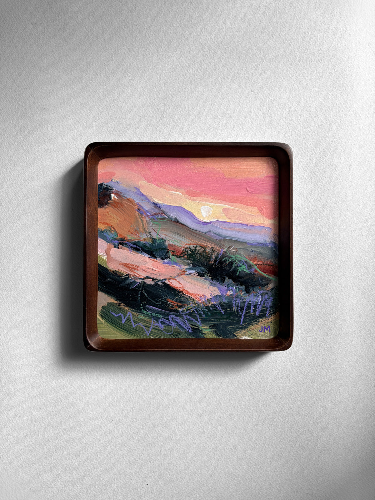 A square framed landscape painting featuring a colorful sunset scene with pink, orange, purple, and green brushstrokes, mounted on a light gray wall.