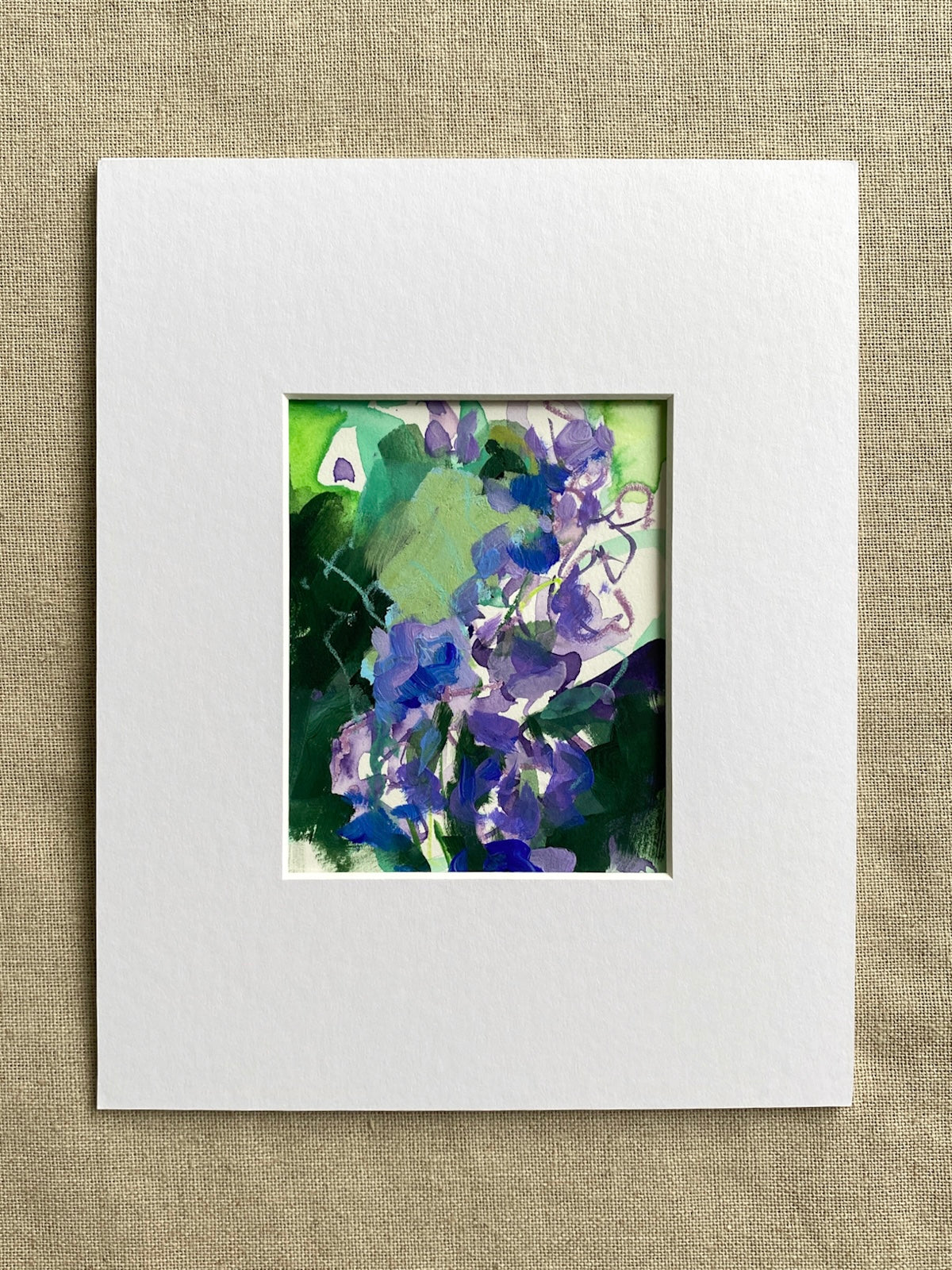 Purple and green matted floral artwork on a textured beige surface