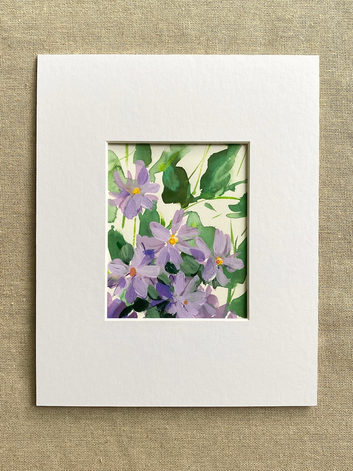 Matted artwork of purple flowers and green leaves on a textured beige background