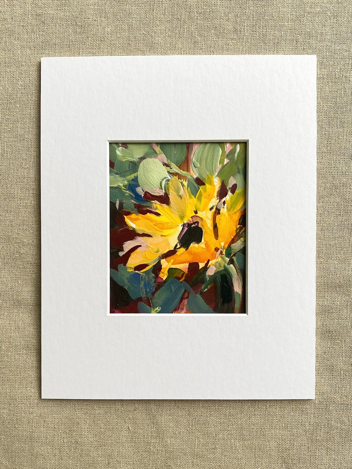 Matted artwork of a sunflower and green leaves on a textured beige background